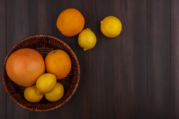 Vista superior de limones con naranjas y pomelos con canasta sobre fondo de madera