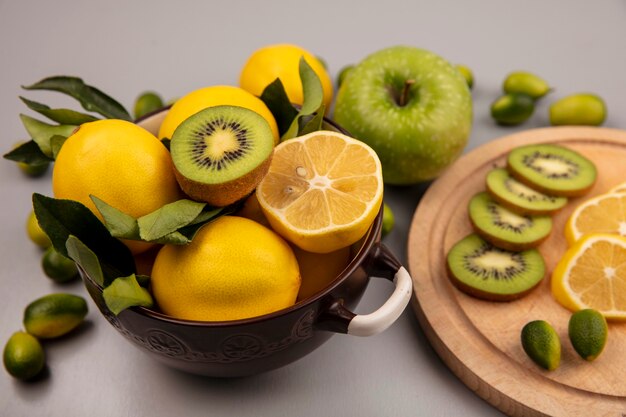 Vista superior de limones en un recipiente con kiwi y rodajas de limón sobre una tabla de cocina de madera con kinkans y manzana aislado en una pared blanca