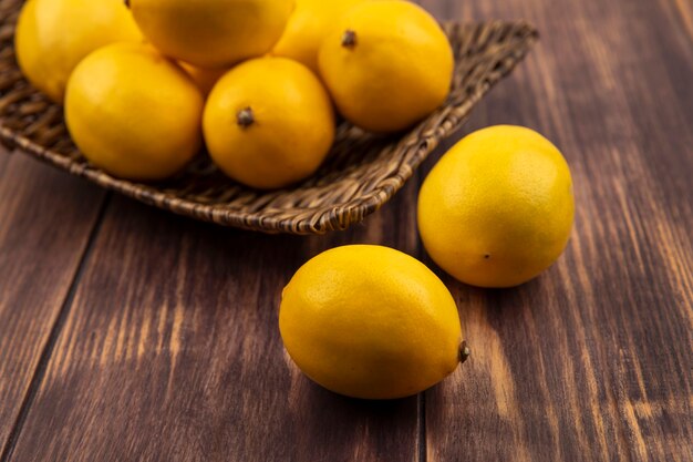 Vista superior de limones saludables en una bandeja de mimbre con limones aislado en una pared de madera