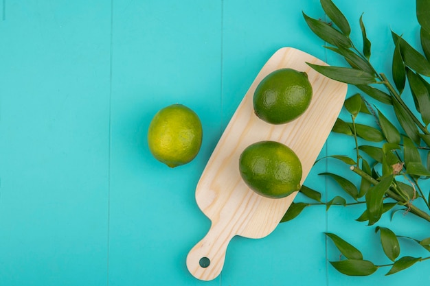 Vista superior de limones verdes frescos en tablero de cocina de madera con hojas en azul con espacio de copia