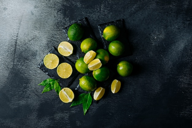 Vista superior de limones verdes con rodajas sobre fondo negro con textura. horizontal