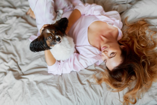 Vista superior. Lindo juguetón cachorro mirando y sentado en la cama con linda chica de jengibre.
