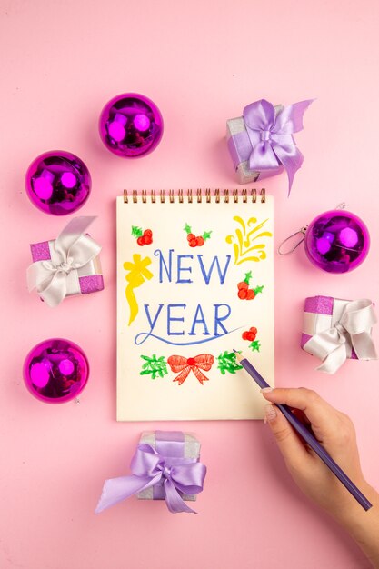 Vista superior lindos regalos con juguetes de árbol de Navidad y nota de año nuevo sobre fondo rosa