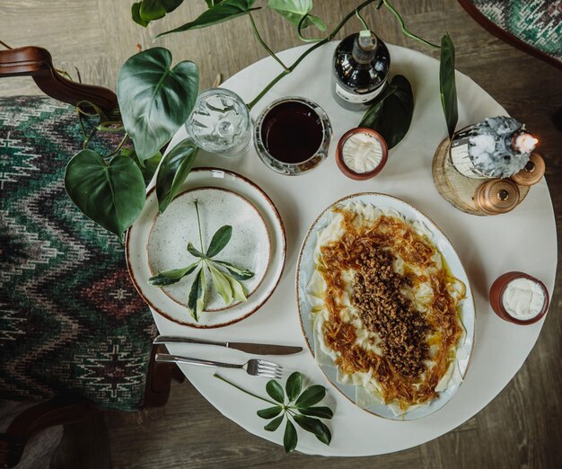 Vista superior de la lista tradicional azerbaiyana khingal en el plato con yogurt agrio en una olla de barro sobre una mesa blanca