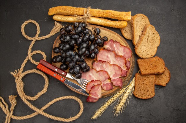 Vista superior de lonchas de jamón con uvas y rebanadas de pan sobre el fondo oscuro