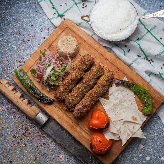 Vista superior lula kabab con verduras fritas y cebolla picada y cuchillo y ayran en tabla de cortar