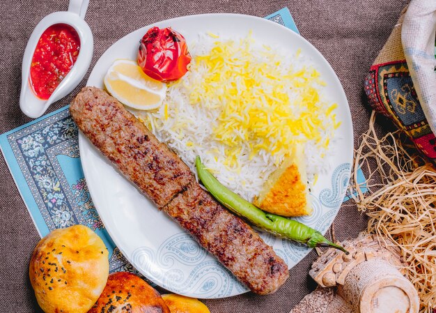 Vista superior de lula kebab con arroz con tomate y pimiento verde a la parrilla con una rodaja de limón y salsa