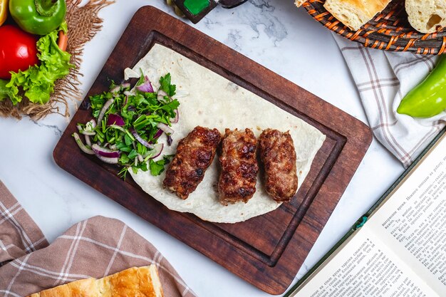 Vista superior de lula kebab con cebolla roja y hierbas en lavash sobre una tabla de madera