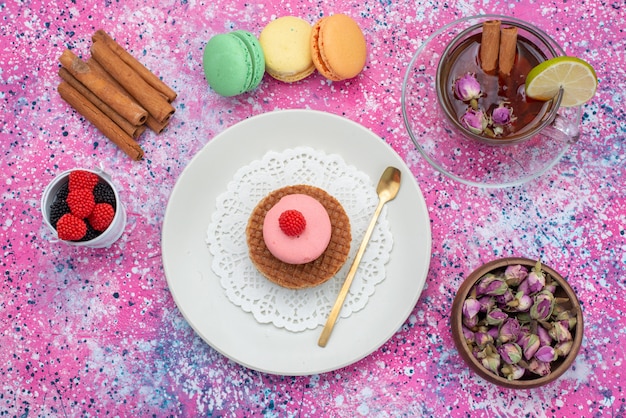 Vista superior de macarons franceses con bayas de canela y té en el fondo colorido pastel galleta azúcar color dulce hornear