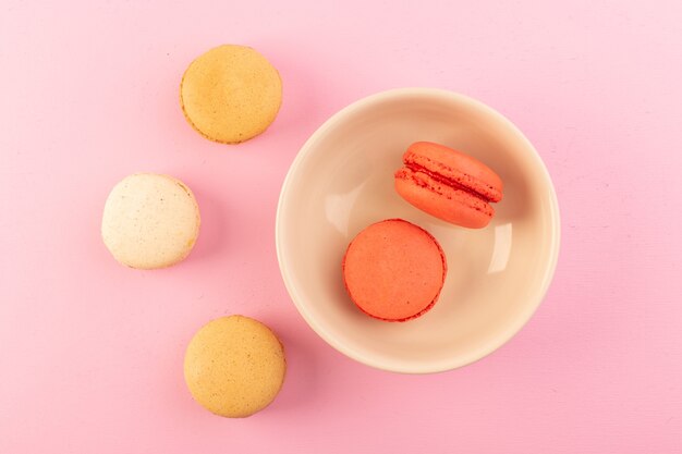 Una vista superior de macarons franceses de color dentro y fuera de la placa en la mesa rosa pastel galleta azúcar dulce