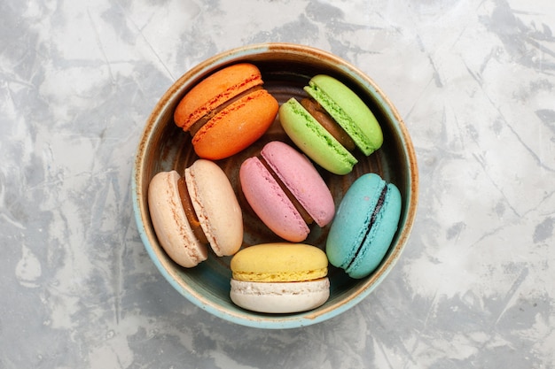 Vista superior macarons franceses coloreados deliciosos pasteles en superficie blanca