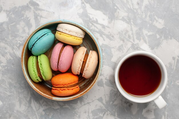 Vista superior de macarons franceses coloreados deliciosos pasteles con taza de té en la superficie blanca
