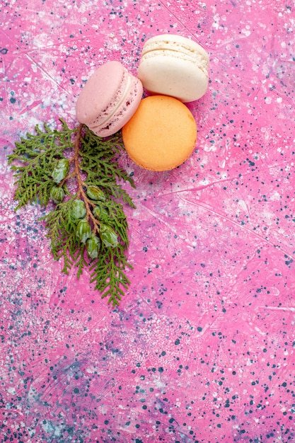 Vista superior macarons franceses deliciosos pasteles en superficie rosa