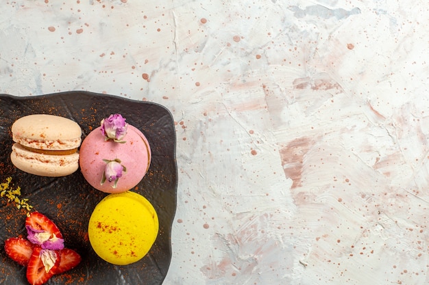 Vista superior de macarons franceses dentro de la placa en el piso blanco pastel de galletas fruta dulce
