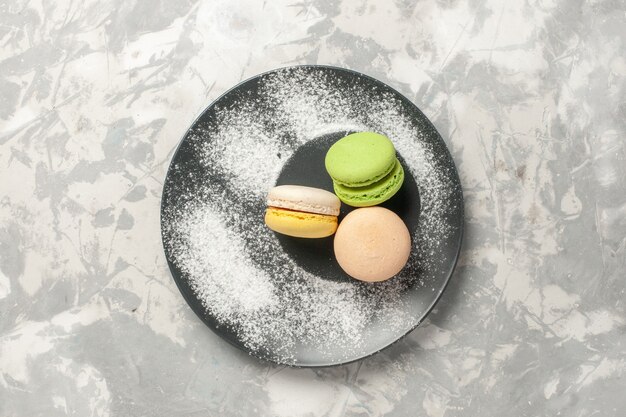 Vista superior macarons franceses dentro de la placa en superficie blanca pastel de azúcar hornear galletas galletas de té dulce
