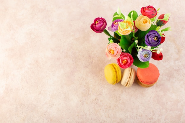 Una vista superior de macarons franceses con flores sobre la mesa rosa pastel galleta azúcar dulce