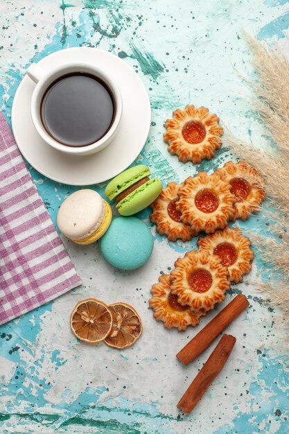 Vista superior de macarons franceses con galletas y taza de té en la superficie azul