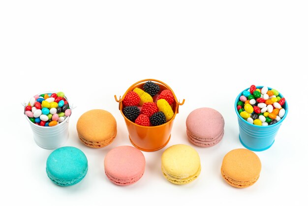 Una vista superior de macarons franceses junto con coloridos caramelos y mermeladas en blanco, arco iris de caramelo de color