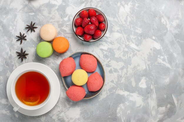 Vista superior de macarons franceses con pequeños pasteles y una taza de té en la superficie blanca pastel galleta azúcar pastel dulce té