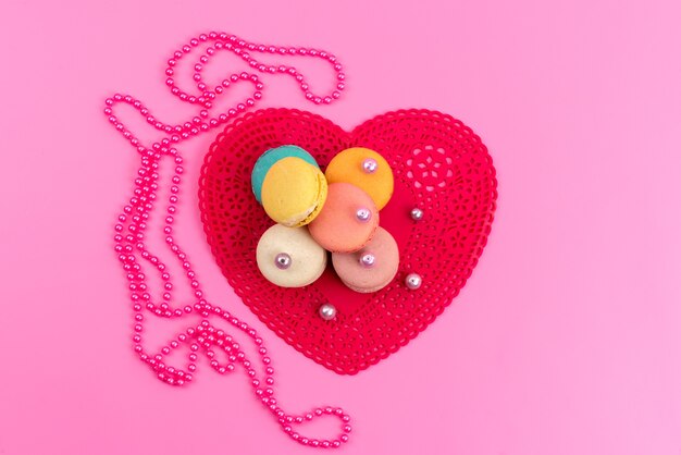 Una vista superior de macarons franceses redondos deliciosos junto con forma de corazón rojo en rosa, pastel de galleta dulce