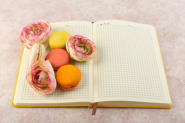 Una vista superior de macarons franceses con rosas en el cuaderno y pastel de mesa rosa galleta dulce de azúcar