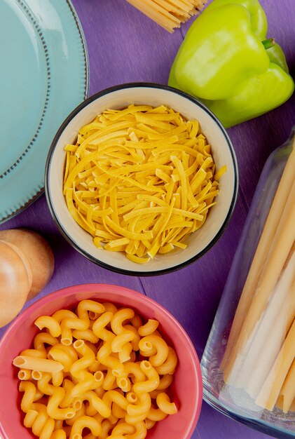 Vista superior de macarrones como cavatappi bucatini tagliatelle con pimiento y plato sobre superficie morada