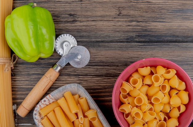 Vista superior de macarrones como ziti y pipe-rigate en cuencos con pimienta sobre superficie de madera