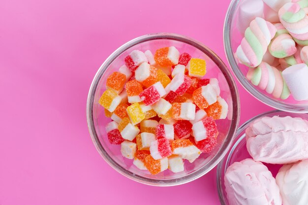 Una vista superior de malvaviscos blanco-rosa dulces y pegajosos junto con coloridos caramelos de azúcar en rosa