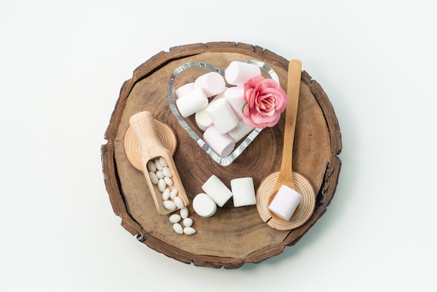 Una vista superior de malvaviscos blancos deliciosos y dulces en un escritorio de madera marrón, en un escritorio blanco, dulces dulces