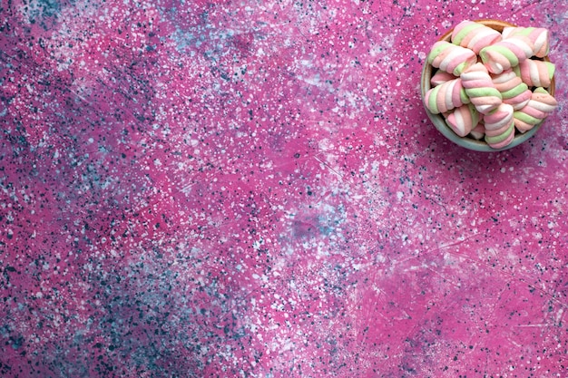 Vista superior de malvaviscos de colores dulces poco formados dentro de una olla redonda sobre la superficie rosa