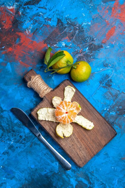 Vista superior de mandarina pelada en tabla de cortar cuchillo de cena mandarinas frescas con hojas en superficie azul lugar libre
