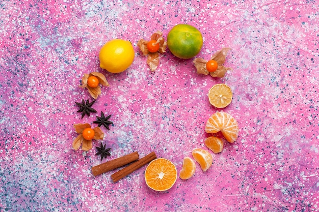 Vista superior de mandarinas agrias frescas con limones y canela sobre el fondo rosa claro.