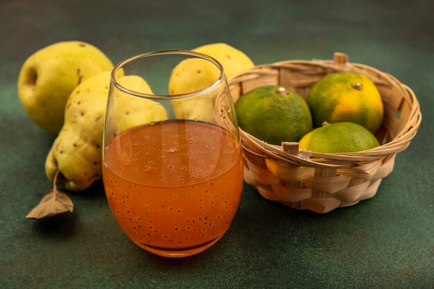 Vista superior de mandarinas frescas en un balde con membrillos y un vaso de jugo de fruta fresca