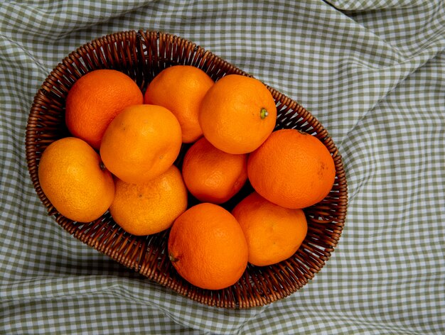 Vista superior de mandarinas frescas maduras en una cesta de mimbre sobre tela escocesa