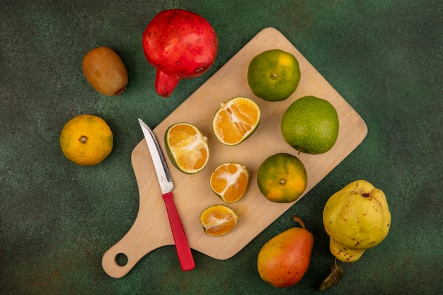 Vista superior de mandarinas frescas en una tabla de cocina de madera con un cuchillo con deliciosas frutas como la granada de pera