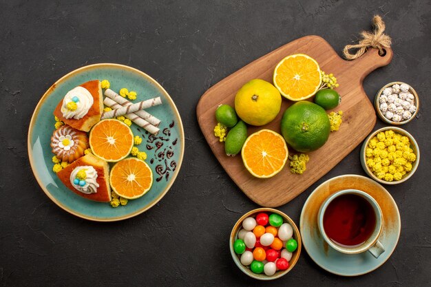 Vista superior de mandarinas frescas con taza de té y dulces en negro