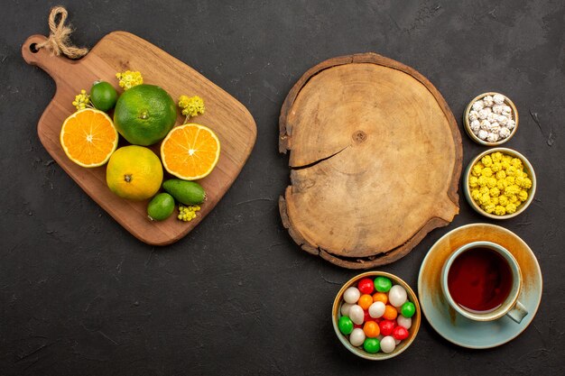 Vista superior de mandarinas frescas con taza de té y dulces en negro