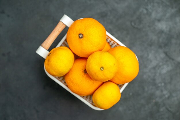 Vista superior de mandarinas y naranjas en canasta de plástico sobre fondo oscuro