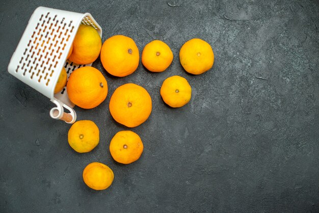 Vista superior de mandarinas y naranjas esparcidas desde la canasta de plástico sobre fondo oscuro