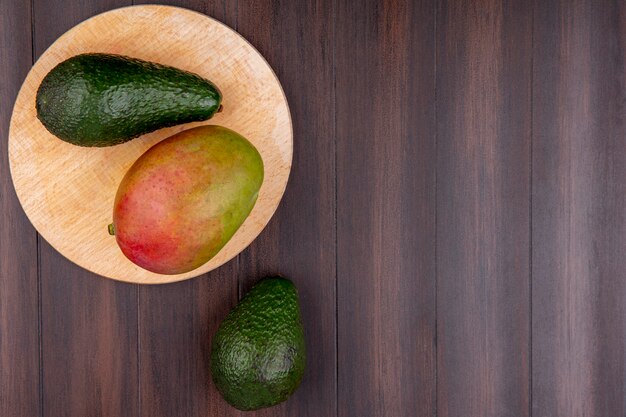 Vista superior de mango con aguacate sobre una tabla de cocina de madera sobre una superficie de madera