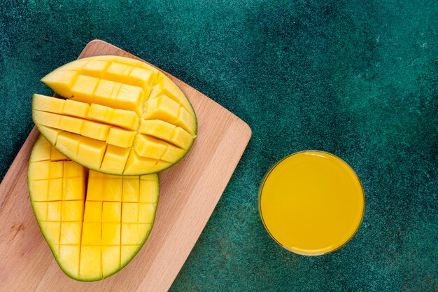 Vista superior de mango en rodajas en una pizarra con un vaso de jugo de naranja sobre una mesa verde