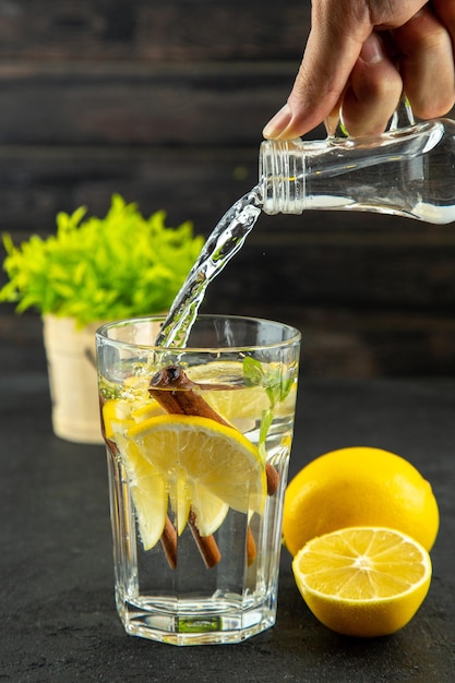 Vista superior de la mano agregando un vaso líquido de agua con limas de limón y canela sobre fondo negro con espacio libre