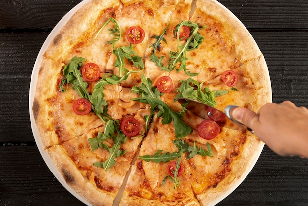 Vista superior de la mano con cortador de pizza en deliciosa pizza
