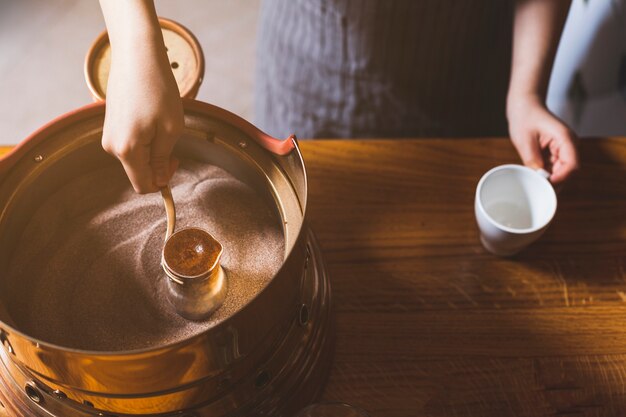 Vista superior de la mano femenina que prepara café turco en arena