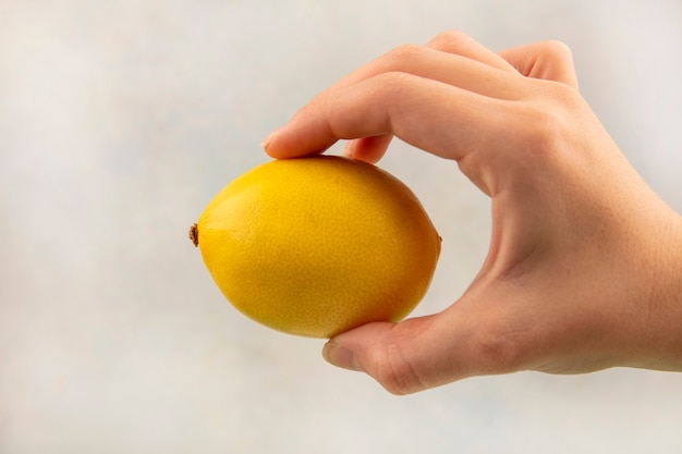 Vista superior de la mano femenina que sostiene el limón de cítricos sobre una superficie blanca