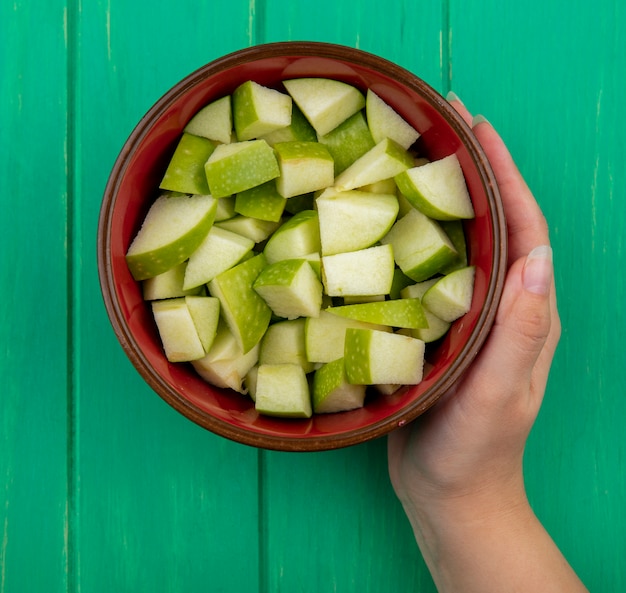 Vista superior de la mano femenina sosteniendo un cuenco rojo de manzanas picadas en verde