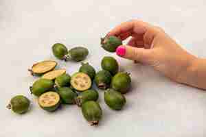 Foto gratuita vista superior de la mano femenina sosteniendo una feijoa madura saludable con feijoas aislado en una pared gris