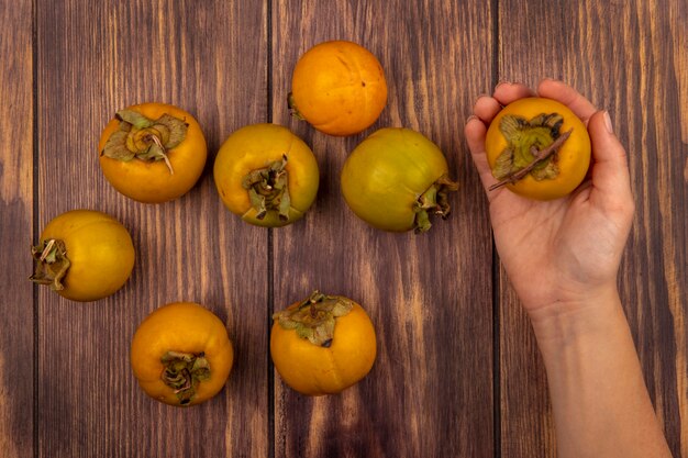 Vista superior de la mano femenina sosteniendo una fruta de caqui naranja fresca en una mesa de madera