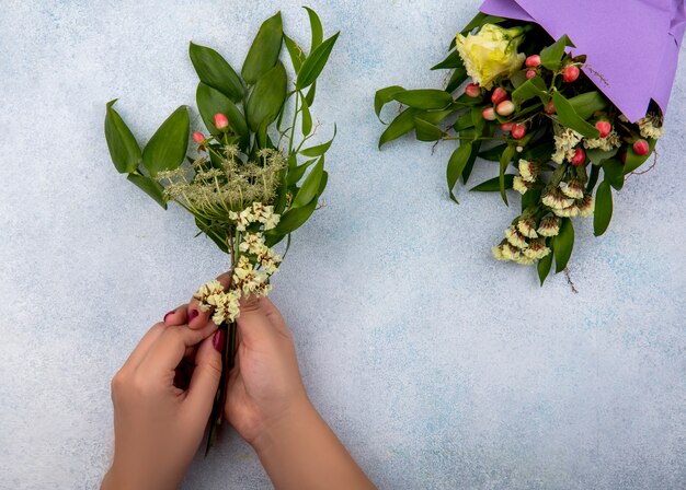 Vista superior de la mano femenina sosteniendo hojas con bayas con ramo de flores aislado en blanco