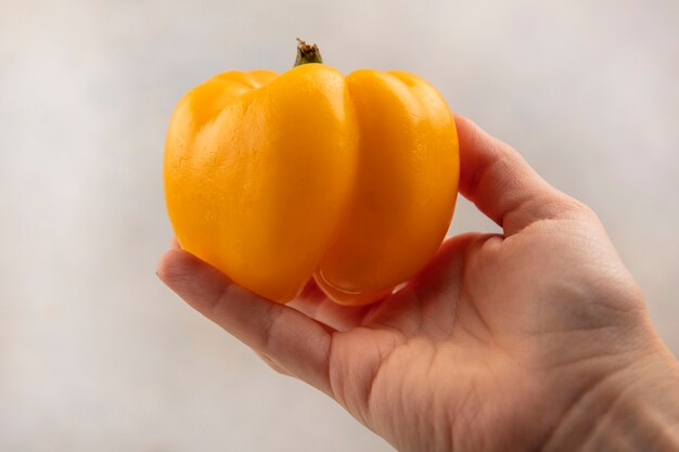 Vista superior de la mano femenina sosteniendo un pimiento amarillo fresco sobre una superficie blanca